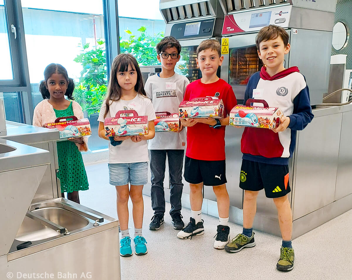 Eine Gruppe von Kindern hält DB-Kindermenü-Boxen in einer Küche der Versuchsküche der Bahn.